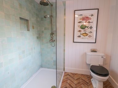 A bathroom with a tiled shower area a toilet with a black seat and a framed fish illustration on the wall at The Old Rectory Coach House in Rathmullan County Donegal