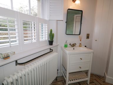 A bathroom with a white sink unit a mirror a radiator and a window with shutters at The Old Rectory Coach House in Rathmullan County Donegal
