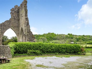 A stone ruin with archways next to a green hedge and grassy area at Heron House in Talley near Llandeilo