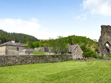 Stone buildings and a stone wall with trees and hills in the background at Heron House in Talley near Llandeilo