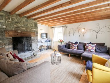A living room with wooden beams on the ceiling a stone fireplace sofas a yellow armchair a round coffee table and a window at Heron House Talley near Llandeilo
