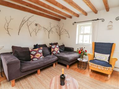 A living room with a dark sectional sofa yellow armchair and a small table with flowers at Heron House Talley near Llandeilo