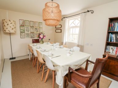 A dining room with a long table set for tea surrounded by chairs a bookshelf and a floor lamp at Heron House Talley near Llandeilo