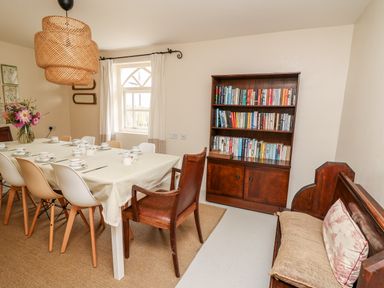 A dining room with a table set for tea surrounded by chairs a bookshelf filled with books and a wooden bench with cushions at Heron House Talley near Llandeilo
