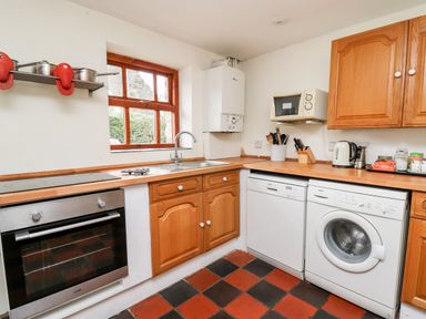 A kitchen with wooden cabinets a stainless steel oven dishwasher washing machine microwave and a window at Heron House in Talley near Llandeilo