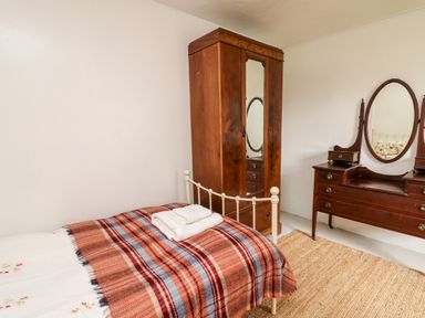 A bedroom with a bed, a wooden wardrobe with mirrored door, a wooden dresser with an oval mirror and a rug on the floor at Heron House in Talley near Llandeilo