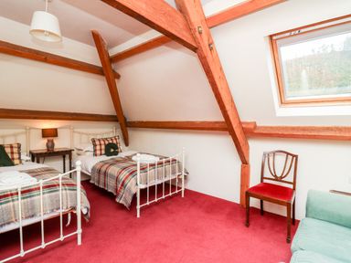 A bedroom with two single beds a wooden chair a green sofa and a window in a room with exposed wooden beams at Heron House Talley near Llandeilo
