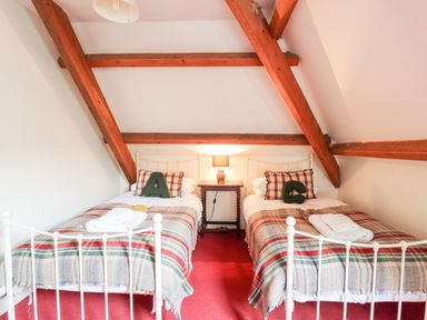 A bedroom with two single beds a bedside table with a lamp and wooden beams on the ceiling at Heron House in Talley near Llandeilo