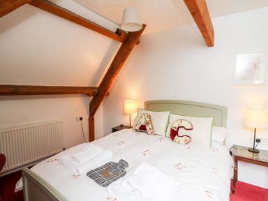A bedroom with a double bed white bedding and floral cushions and wooden beams at Heron House Talley near Llandeilo
