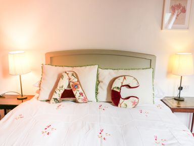 A bedroom with a bed with floral pillows and letter cushions on it with two bedside tables and lamps at Heron House in Talley near Llandeilo