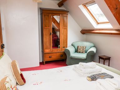 A bedroom with a bed folded towels an armchair wooden wardrobe and a skylight window at Heron House Talley near Llandeilo