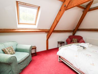 A bedroom with two armchairs a bed and a skylight window at Heron House in Talley near Llandeilo