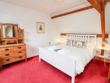 A bedroom with a white bed with floral pillows and white towels on a red carpet at Heron House in Talley near Llandeilo