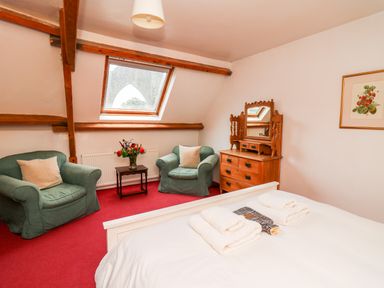 A bedroom with two green armchairs a wooden dresser with mirror a skylight window and a bed with towels at Heron House in Talley near Llandeilo