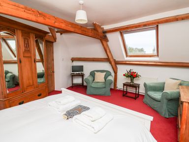 A bedroom with a white bed and folded towels two green armchairs a wooden wardrobe and a small table with flowers at Heron House in Talley near Llandeilo