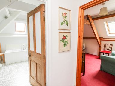A hallway showing a bathroom with a bathtub and skylight and a room with wooden beams chairs and red carpet at Heron House in Talley near Llandeilo