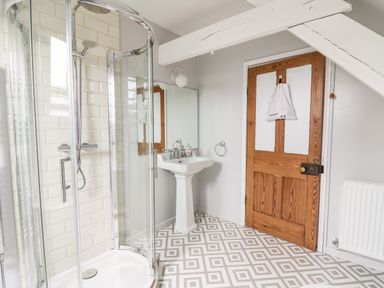 A bathroom with a corner shower cubicle a pedestal sink wooden door and patterned floor at Heron House in Talley near Llandeilo
