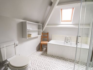 A bathroom with a toilet wooden chair bathtub window and tiled floor at Heron House in Talley near Llandeilo