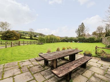 A wooden picnic table and benches on a stone patio with a grassy field and hills in the background at Heron House in Talley near Llandeilo