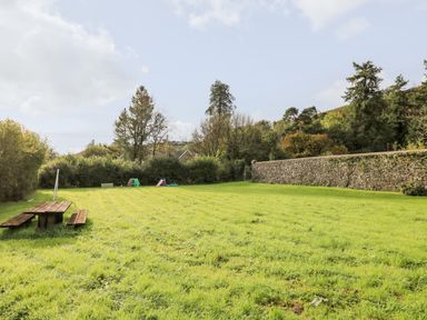 A grassy garden area with a picnic table and children's play equipment surrounded by trees and a stone wall at Heron House in Talley near Llandeilo