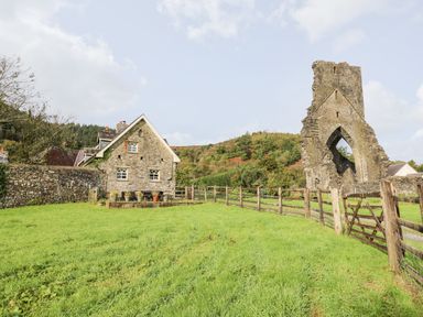 A stone house and the ruins of an arched stone building in a grassy yard with a wooden fence at Heron House in Talley near Llandeilo