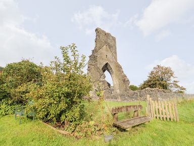 A stone ruin of an old building with an arch next to a wooden bench and bushes in a grassy field at Heron House in Talley near Llandeilo