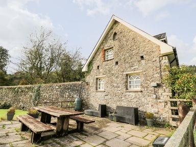 A stone cottage with two small outdoor black chairs and a wooden picnic table on a paved patio at Heron House in Talley near Llandeilo