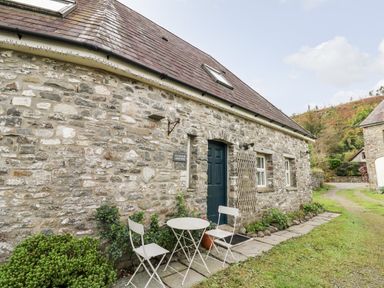 A stone cottage with a dark door and two white chairs and a round table outside on a stone path at Heron House Talley near Llandeilo