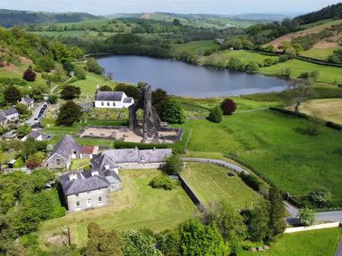 A rural area with historic church ruins near a lake surrounded by green fields and houses at Buzzards Watch in Talley near Llandeilo