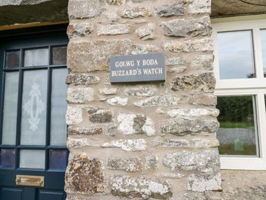 A stone wall with a sign reading Buzzards Watch next to a door and window at Buzzards Watch Talley near Llandeilo