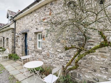 A stone cottage exterior with a small round table and two chairs outside and a leafless tree at Buzzards Watch in Talley near Llandeilo