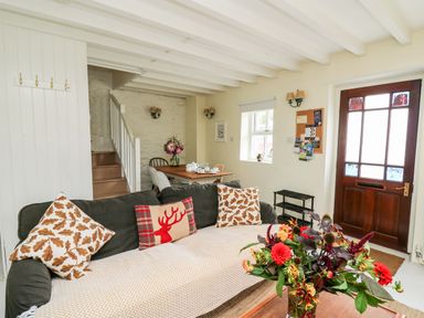A living room with a sofa and cushions a dining table with tea set and flowers and a wooden door at Buzzards Watch in Talley near Llandeilo