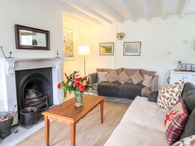 A living room with a fireplace a wooden table with flowers two sofas and framed pictures on the wall at Buzzards Watch in Talley near Llandeilo