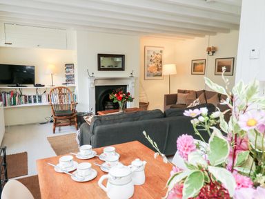 A living room with black sofas a fireplace a wooden chair a television and a table set for tea with flowers at Buzzards Watch in Talley near Llandeilo