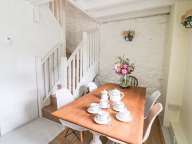 A dining area with a wooden table set with a tea set and flowers near stairs at Buzzards Watch in Talley near Llandeilo