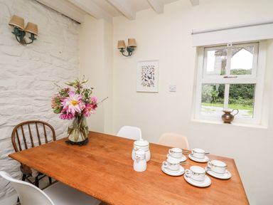 A dining area with a wooden table set with teacups and a vase of flowers near a window at Buzzards Watch Talley near Llandeilo