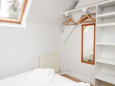 A bedroom corner with a bed and white towels on it a wall-mounted mirror wooden hangers and shelves by a skylight window at Buzzards Watch in Talley near Llandeilo