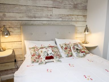 A bed with floral pillows and letter cushions on a white quilt with wooden wall and lamps at Buzzards Watch Talley near Llandeilo