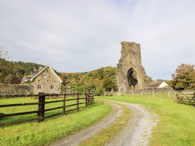 A stone house and a large stone ruin with an arch along a gravel pathway in a grassy rural area at Buzzards Watch in Talley near Llandeilo