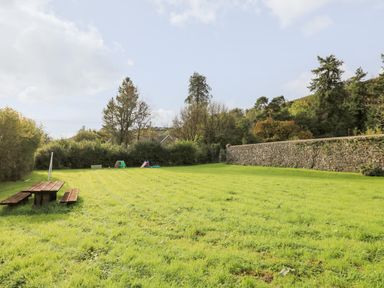 A grassy garden area with a wooden picnic table and children's play equipment at Buzzards Watch Talley near Llandeilo
