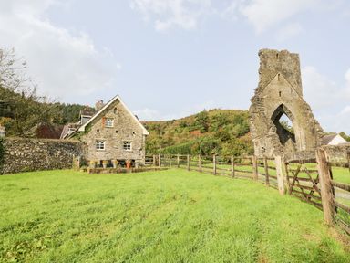 A grassy yard with a stone house and a stone arch ruin near a wooden fence at Buzzards Watch in Talley near Llandeilo