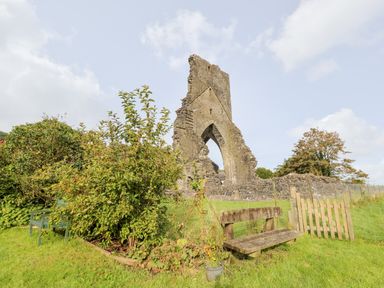 A ruins with an arched stone structure in a grassy field with benches and plants at Buzzards Watch in Talley near Llandeilo