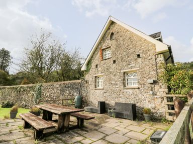 An outdoor patio area with wooden picnic table benches and stone house exterior at Buzzards Watch in Talley near Llandeilo