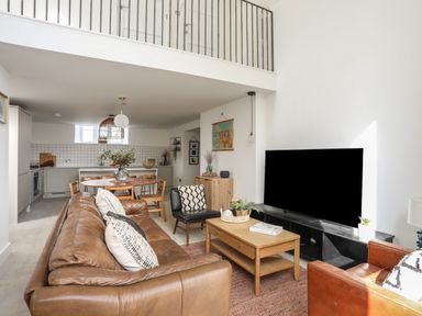 A living room with brown leather sofas a wooden coffee table and a large television with an open kitchen and dining area at Ysgol Fach Little School in Benllech
