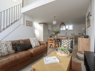 An open living room and kitchen with a brown leather sofa pillows wooden dining table and chairs plants and a wooden coffee table at Ysgol Fach Little School Benllech