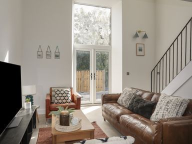 A living room with a leather sofa and armchair a wooden coffee table and large windows at Ysgol Fach (Little School) in Benllech