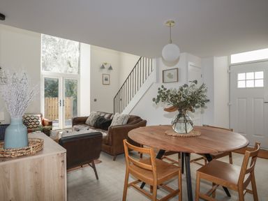 A living room with a round wooden dining table and chairs a leather sofa and large windows at Ysgol Fach Little School in Benllech
