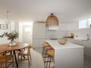 A kitchen with an island and stools a round dining table with chairs and a vase of flowers at Ysgol Fach Little School in Benllech