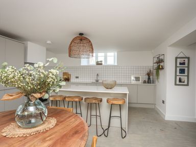 A kitchen with a wooden table and vase of flowers a counter with stools and shelves on the wall at Ysgol Fach in Benllech