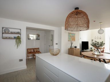 A kitchen island with a bowl and wooden dining table with chairs and a vase at Ysgol Fach Little School in Benllech